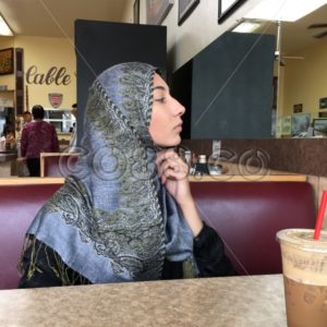 Young Muslim Woman at Coffee Shop wearing an Abaya and looking into Mirror to adjust her Hijab - CO88.co